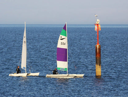 Two small sailboats on open water beside a red navigation marker topped with a compact weather station