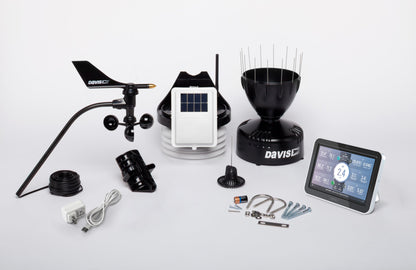 Complete Davis weather station kit laid out with wind sensors, rain collector, solar-panel sensor unit, radiation shield, colour console, cables and mounting hardware